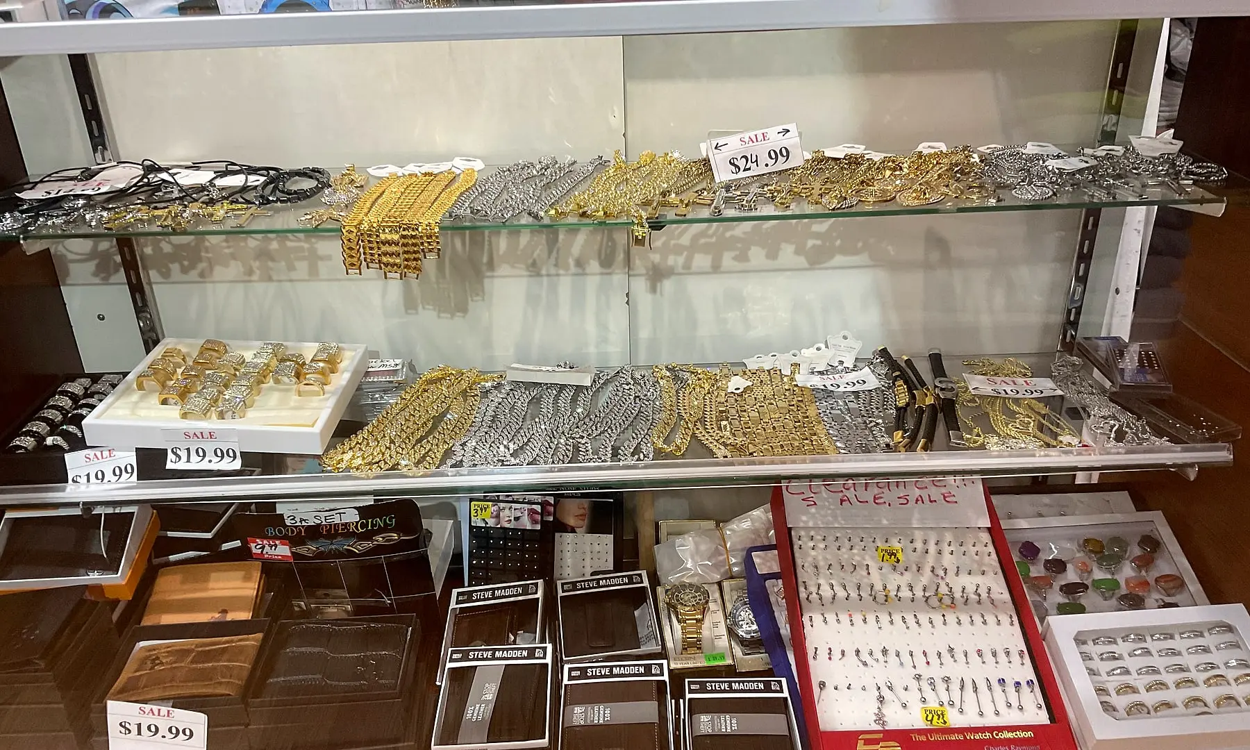 Gold and silver chains and bracelets in a glass case, with earrings and watches below