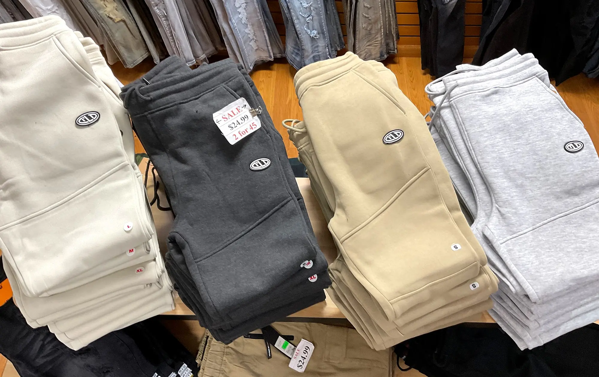 Stacks of fleece joggers in cream, charcoal, khaki, and gray on a display table