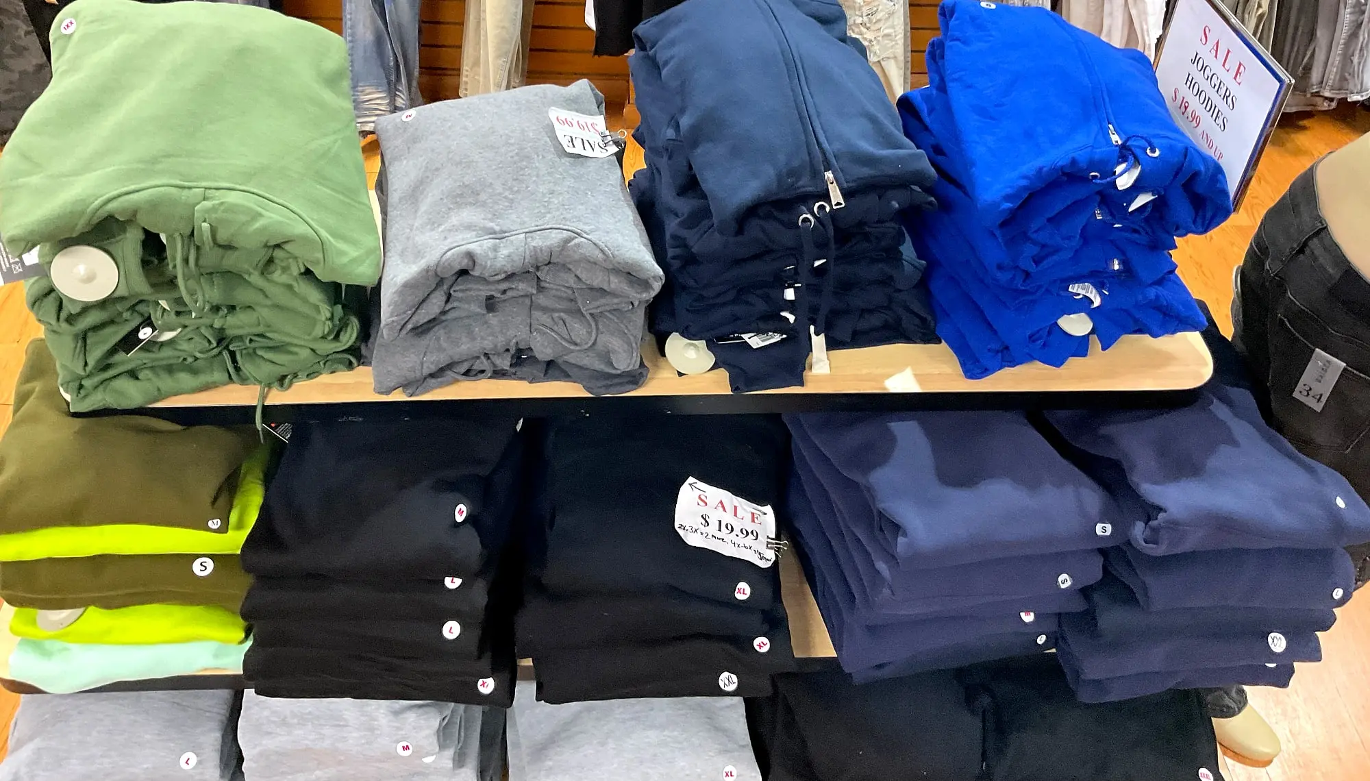A table of folded hoodies in green, gray, navy, and royal blue under a sale sign