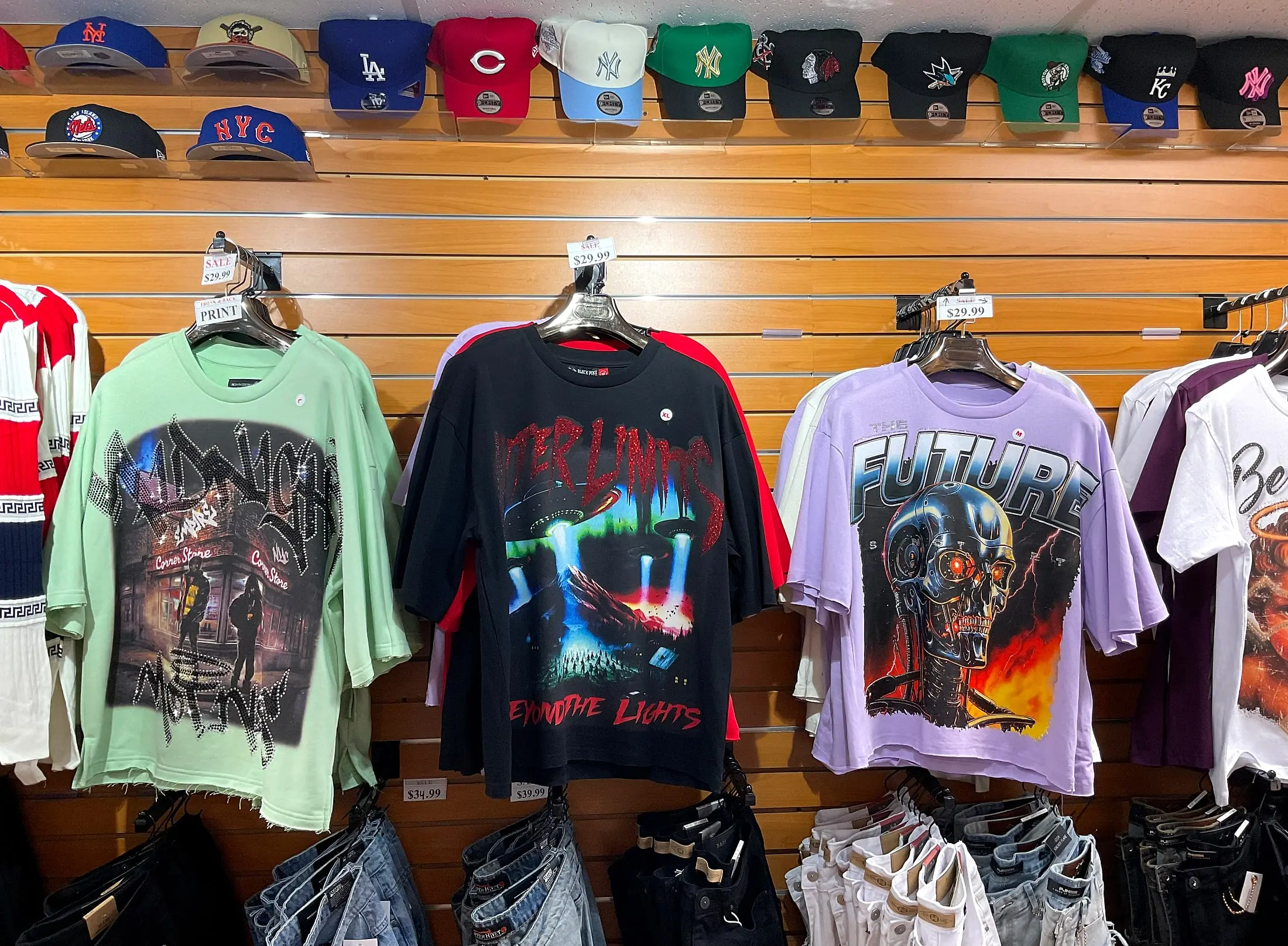 Graphic T-shirts on hangers, with team caps above and jeans below
