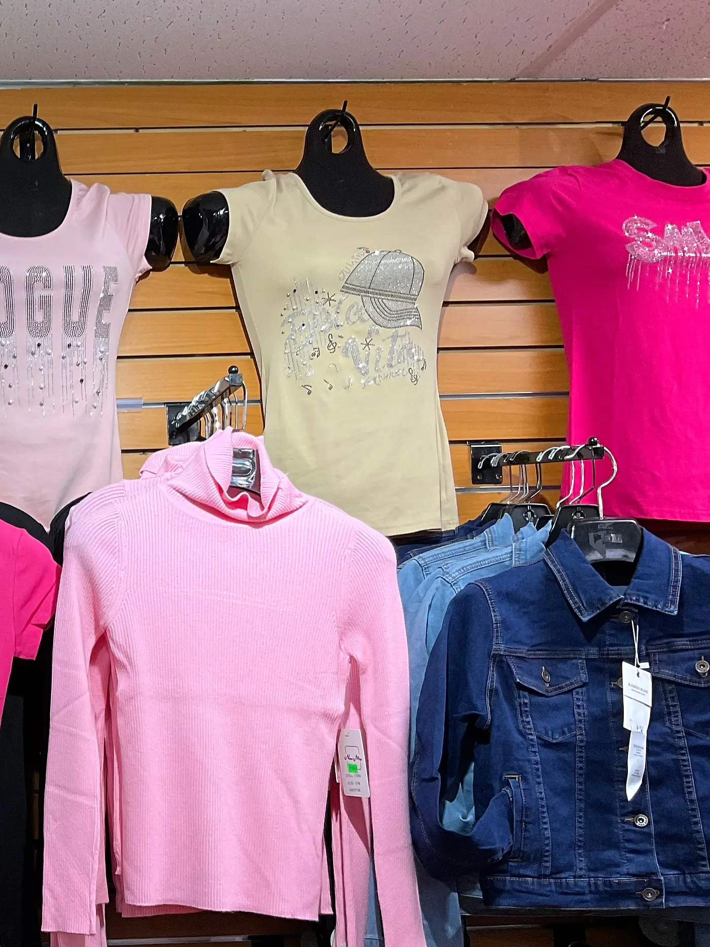 Women's rhinestone T-shirts, a pink turtleneck, and a denim jacket on display
