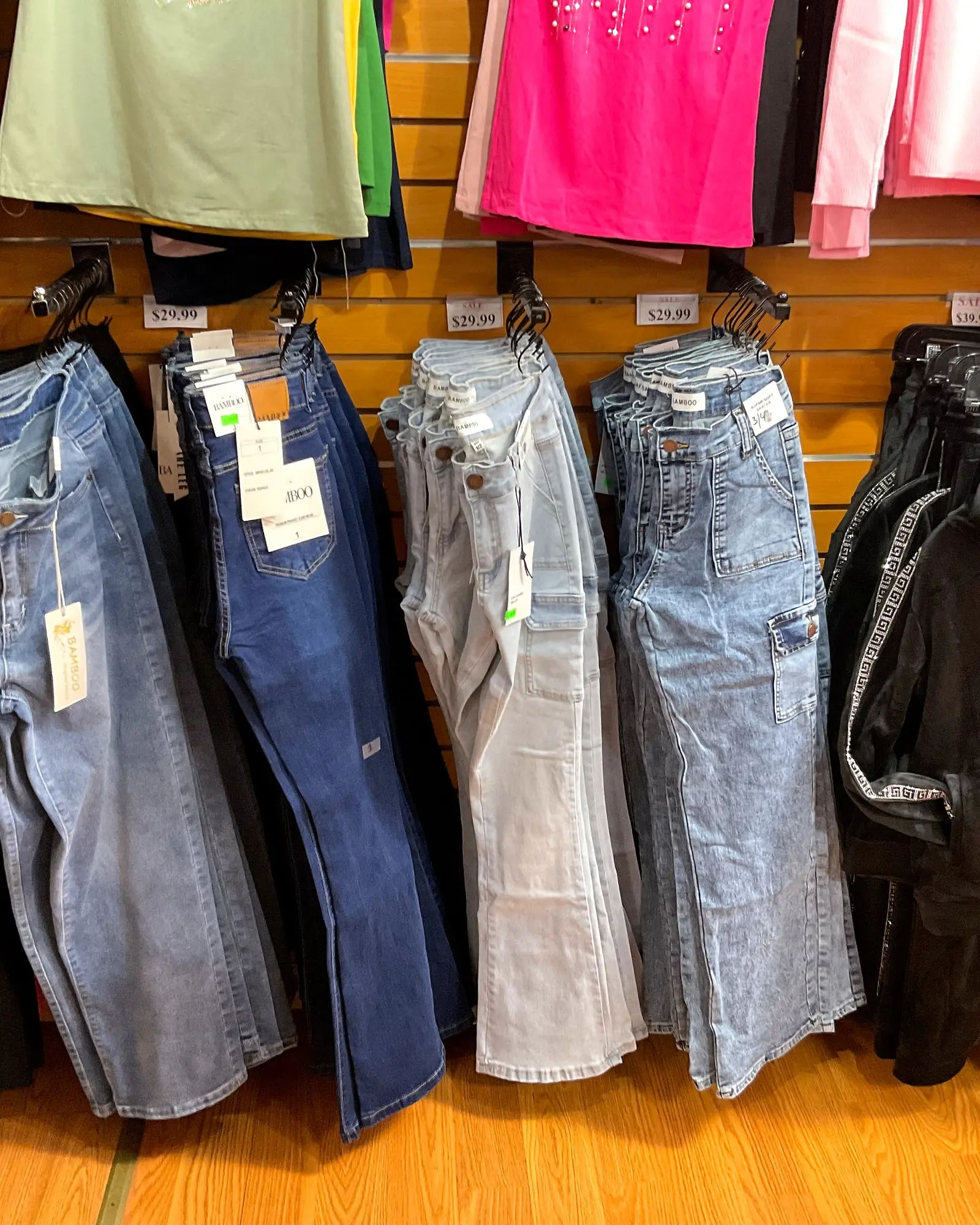 Women's jeans and pants hanging below a row of women's tops