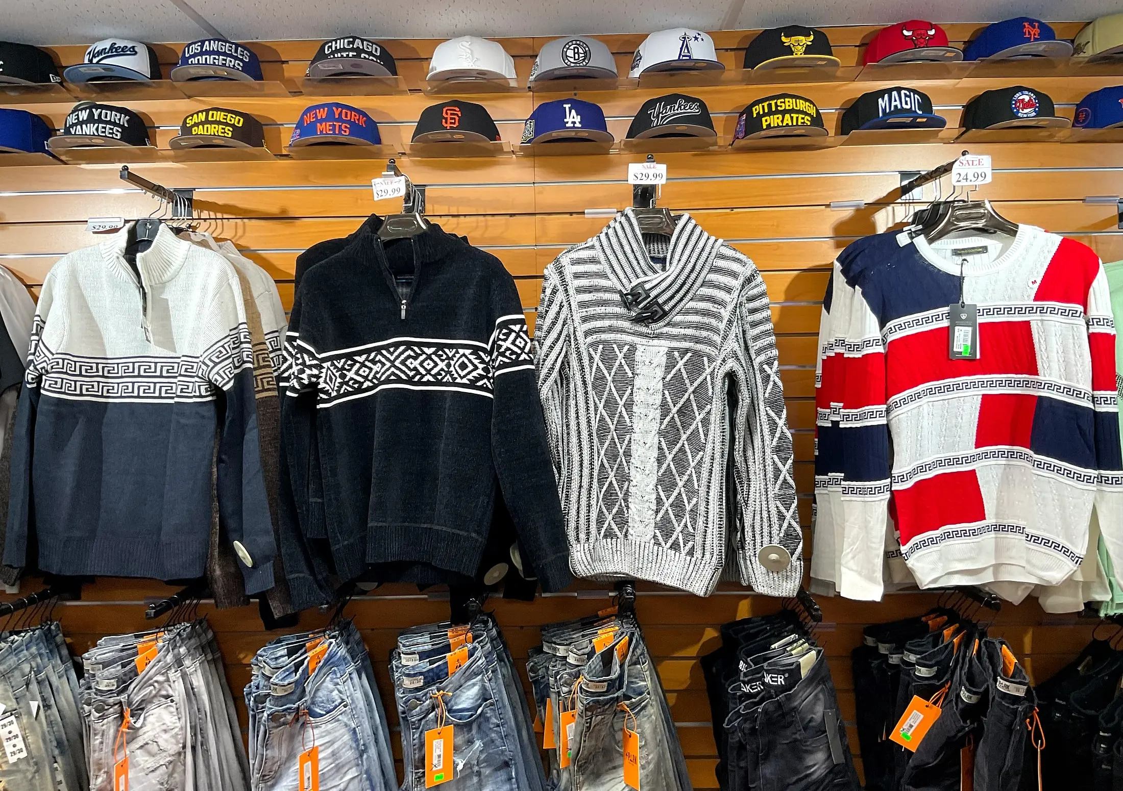Patterned sweaters on the wall, with team caps above and jeans below
