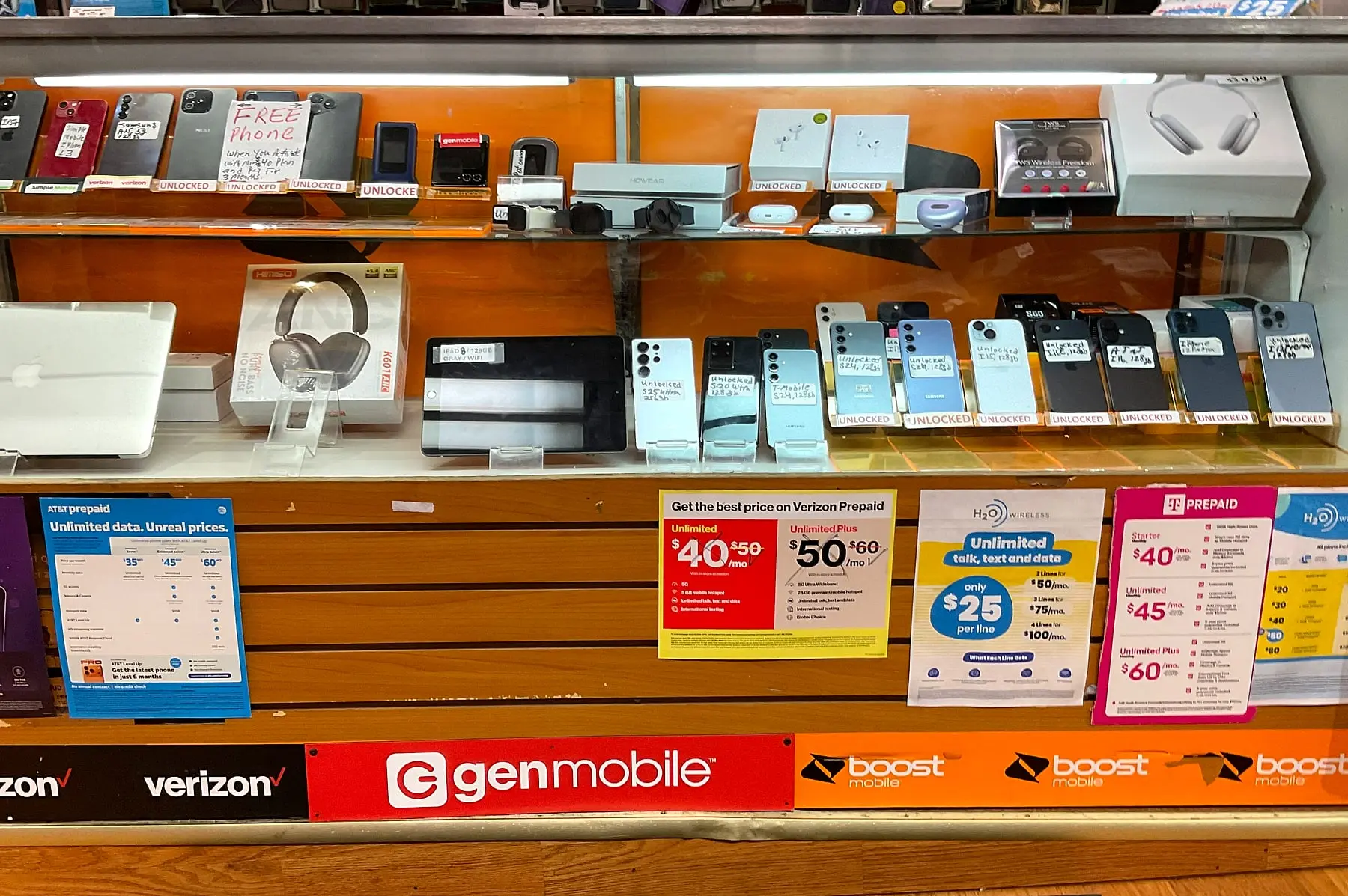 Unlocked phones, earbuds, and headphones in a glass case above prepaid plan signs