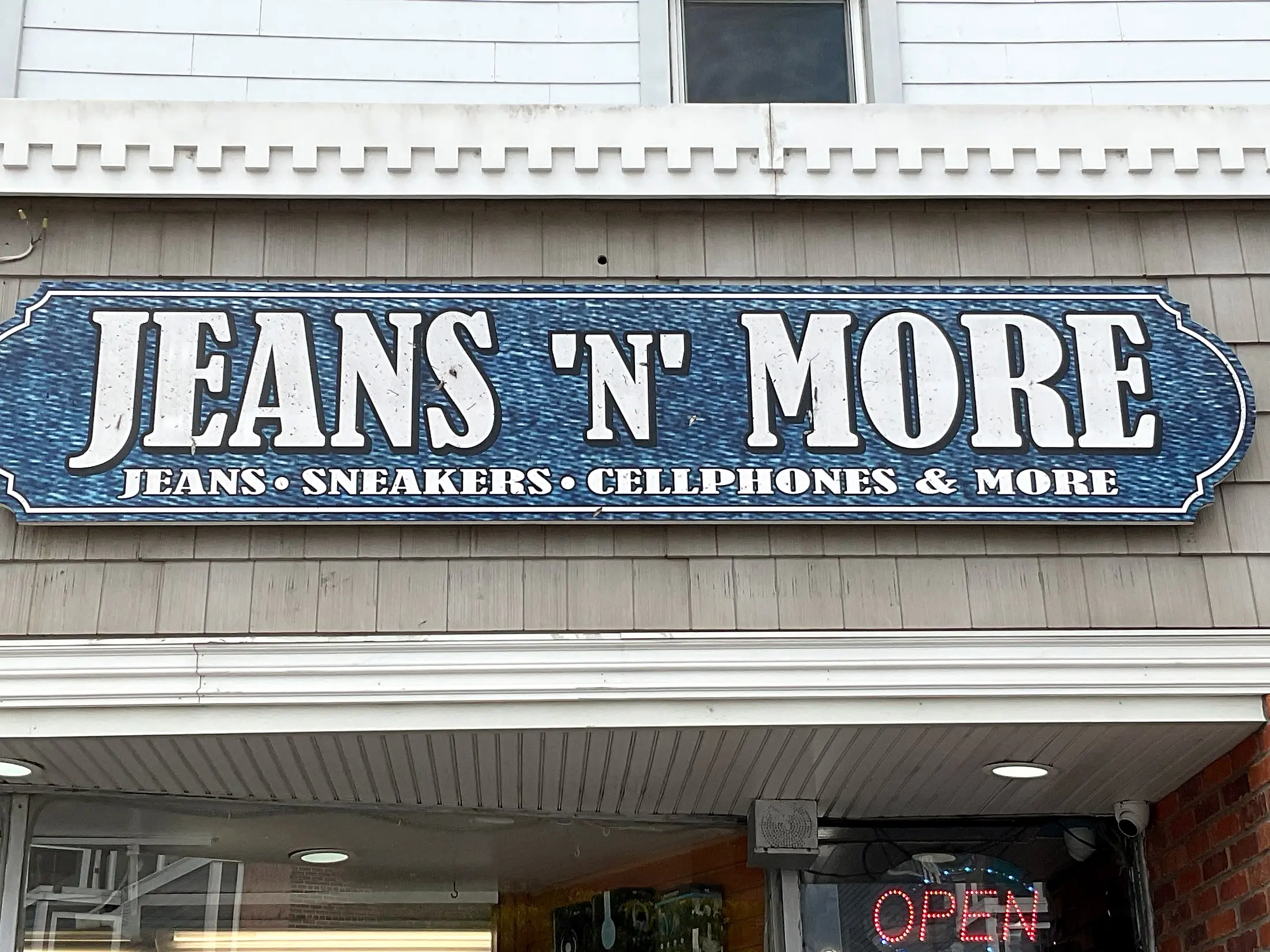 The Jeans ’N’ More store sign reading “Jeans, Sneakers, Cellphones & More” above the entrance