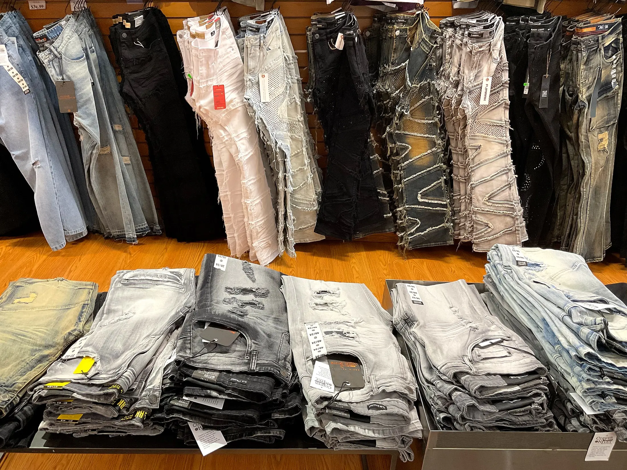 Designer jeans hanging on the wall above tables of folded jeans